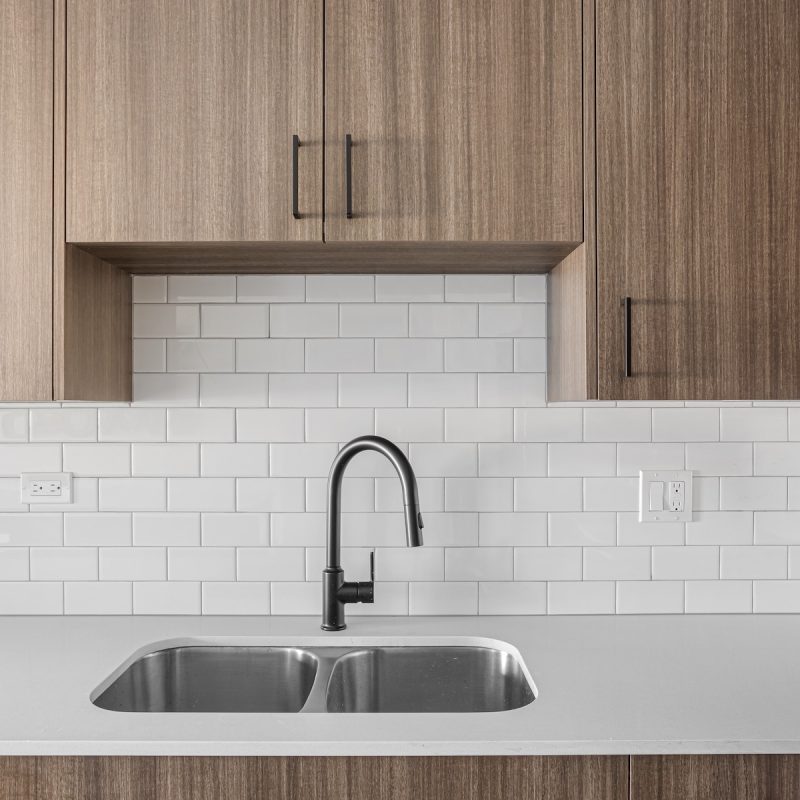 Modern kitchen sink with contemporary faucet and light wood cabinetry at Station 250 apartment interiors Mundelein