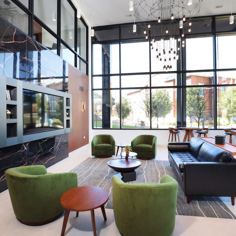 Modern community lounge with green accent chairs, contemporary furniture, and large windows at Station 250 Mundelein